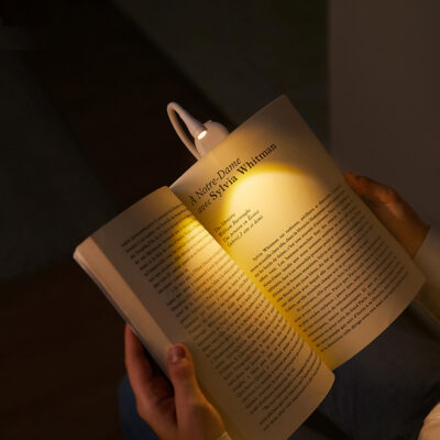 Compact LED clip-on book reading light with a flexible neck illuminating the pages of an open book.