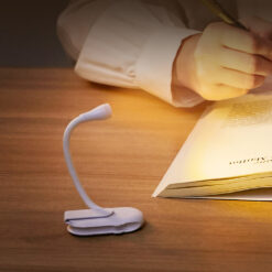 Small black clip-on LED book reading light with a flexible neck attached to a book, illuminating the pages.