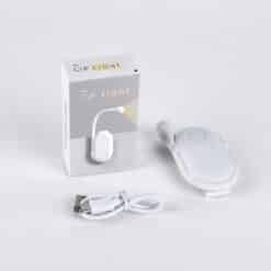 Small black clip-on LED book reading light illuminating pages of an open book in a dimly lit room.