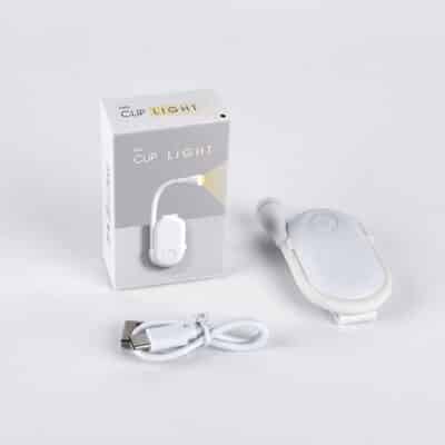 Small black clip-on LED book reading light illuminating pages of an open book in a dimly lit room.