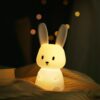 Night Light Soft, squishy silicone bunny lamp with long ears, emitting a warm and gentle glow on a bedside table.