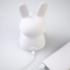 Soft white silicone bunny night light with long ears, glowing with a warm, gentle light against a dark background.